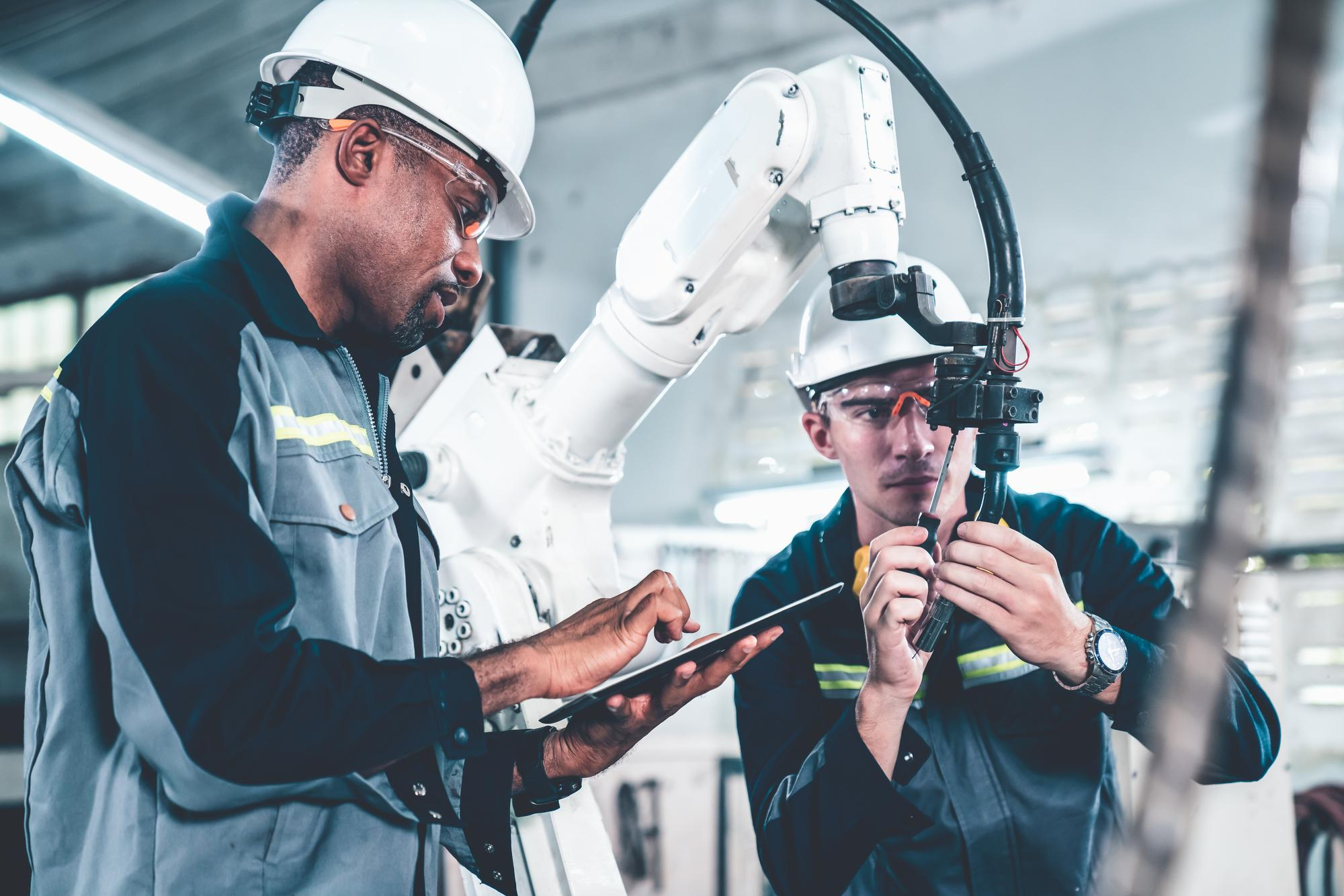 Ingenieurs verzamelen gegevens op tablet en werken aan robotarm in industrieel labo