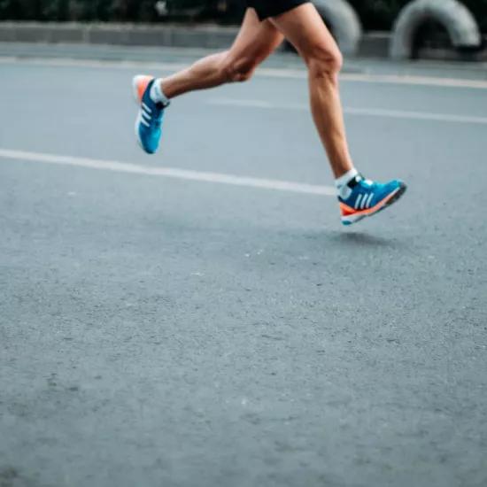 Coureur aux jambes nues et aux chaussures de course bleues claires courant sur une route asphaltée illustrant l'analyse du mouvement de la pression plantaire lors d'exercices de course
