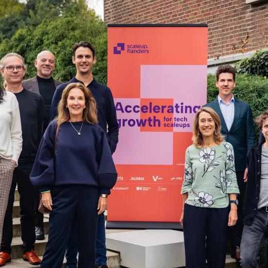 Photo de groupe de l'équipe de Scaleup Flanders, debout devant une bannière avec le texte 'Accelerating growth for tech scaleups.