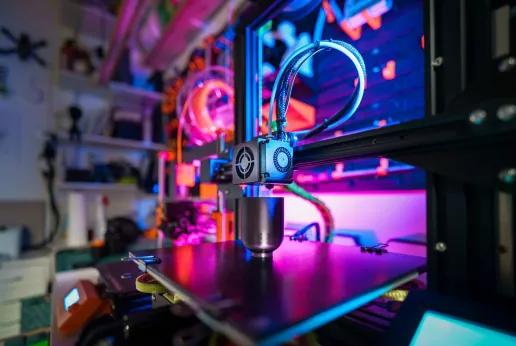 Une imprimante 3D au travail, avec des lumières colorées en arrière-plan, illustrant l'électrification et la fabrication additive en tant que technologies avancées dans les processus de production.