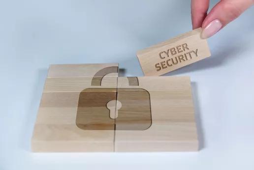 Un puzzle en bois avec un symbole de cadenas gravé, représentant la cybersécurité dans la production avec du bois. Une pièce marquée "CYBER SECURITY" est ajoutée pour compléter le puzzle.