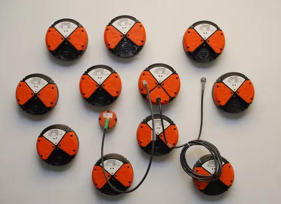 Multiple wireless industrial sensors with orange and black housing mounted on a white background, some connected by cables.